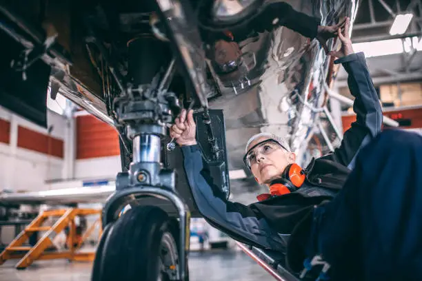 Photo of Elderly female engineer using a socket wrench while repairing or doing maintenance to the landing gear of a small airplane in a maintenance hangar