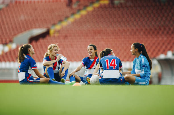 Teenage soccer team relaxing on the grass and communicating. Happy female soccer players talking while sitting on grass after sports training. Copy space. groyne stock pictures, royalty-free photos & images
