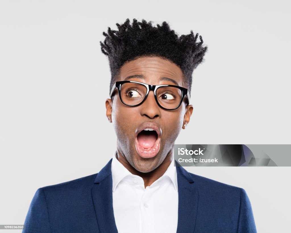 Surprised afro american young businessman Studio portrait of surprised afro american young man in business suit and nerd glasses looking away with mouth open on gray background. Eyeglasses Stock Photo