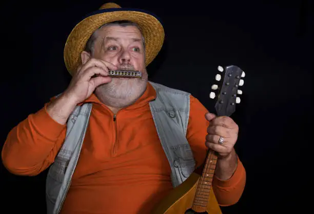 Senior musician playing mouth-organ while holding mandolin