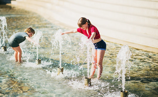 Two happy kids playing in public city fountain on a very hot day