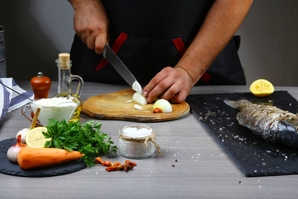 istock Cooking fresh fish for baking by chef hands on wooden table background, cook slicing onion. Authentic lifestyle image 1098247200