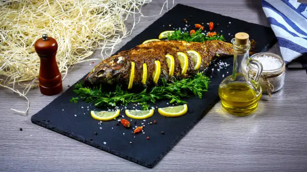 Photo of Grilled river fish on a plate with lemon and baked vegetables and parsley. Food recipe photo, copy text