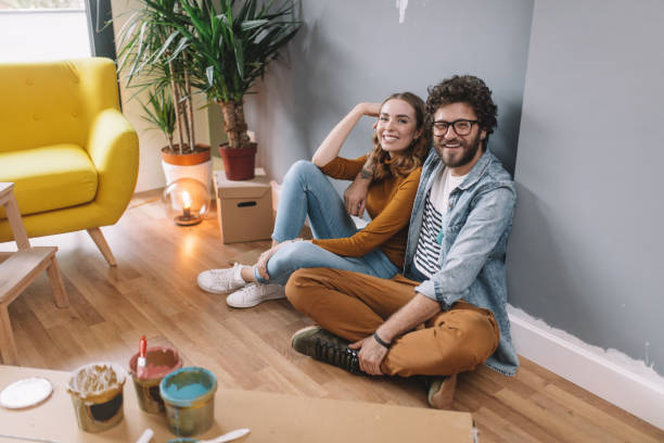 cute couple sitting on the floor in their new home - home addition home improvement paint decorating imagens e fotografias de stock