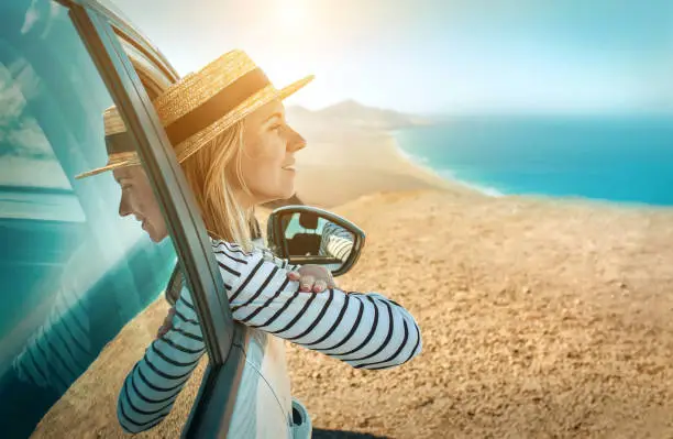 Photo of Happiness young woman sitting in her white car and look on the beautifull ocean coastline view. Freedom, Travell, Journej, Trip concept.