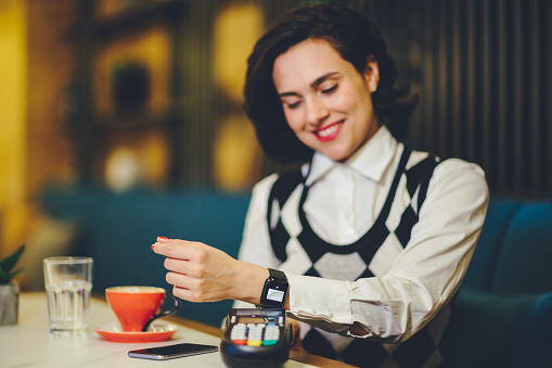 Young woman in cafe paying contactless with smart watch