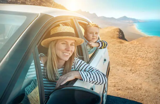 Photo of Happiness mother and son, sitting in white car and look on the beautifull ocean coastline view. Freedom, Family, Travell, Journej, Togetherness concept.