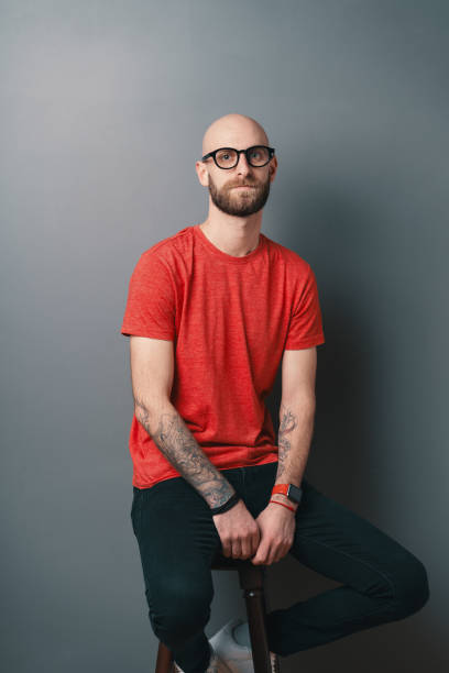 istock Serious young man in red t-shirt posing in the studio on gray background while sitting on a tall chair 1098256972