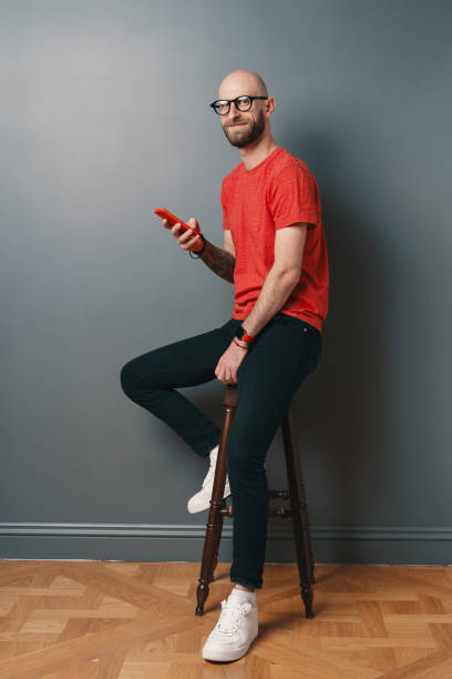 istock Caucasian man with beard, holding a phone in his arm while smiling on gray studio background 1098256982