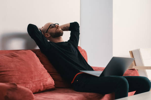 istock Modern man sitting on couch with laptop relaxing with hands behind head 1098257050