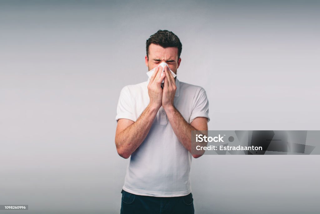 Studio bild från en ung man med näsduk. Sjuka killen isolerade har rinnande näsa. man gör ett botemedel mot förkylning. Nerd bär glasögon - Royaltyfri Nysa Bildbanksbilder