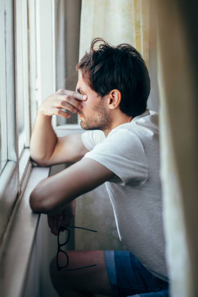istock Tired young man in depression crying near window 1098266490