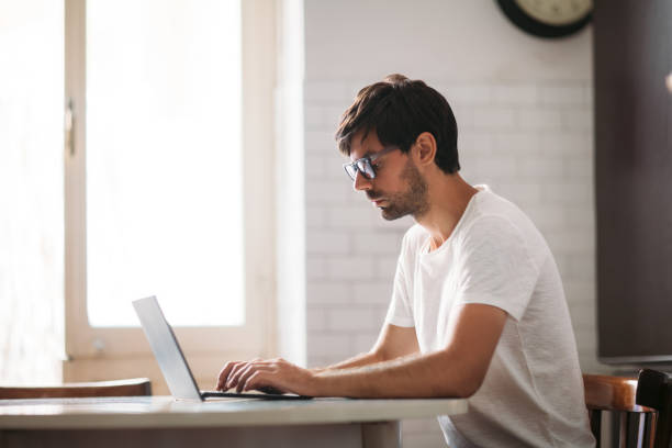 istock Young handsome man in glasses working on laptop in cozy interior 1098266494