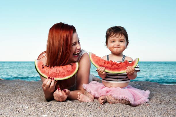 eating delicious watermelon mother with her baby girl lying down on the beach and eating watermelon in summer day. little redhead girl stock pictures, royalty-free photos & images