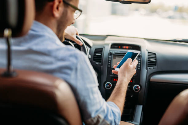 hombre mirando el teléfono móvil mientras se conduce - driving car distracted accident fotografías e imágenes de stock