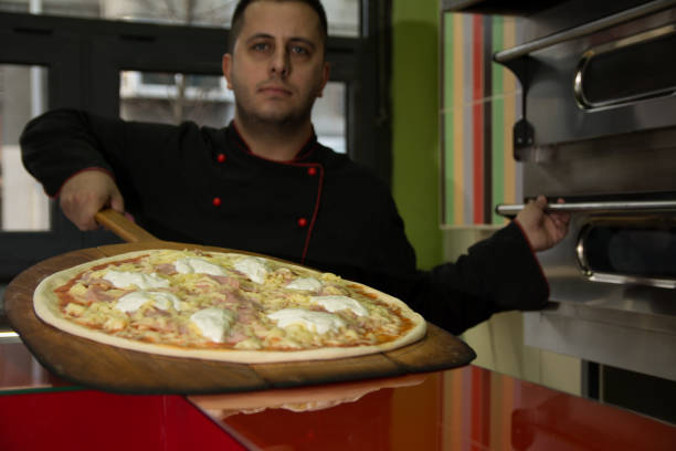 istock Pizza Master in black uniform put pizza in his stainless steel stove - Image 1098272668
