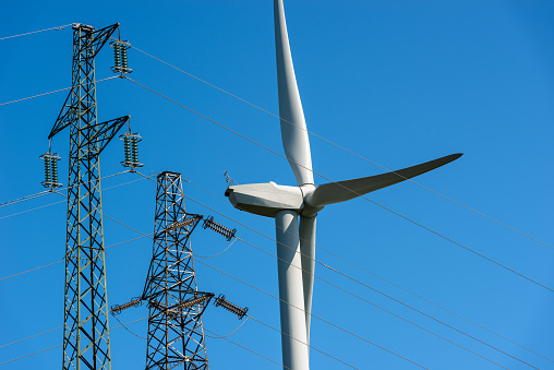 Wind turbine and high voltage towers (power line) on a clear blue sky - Renewable energy concept