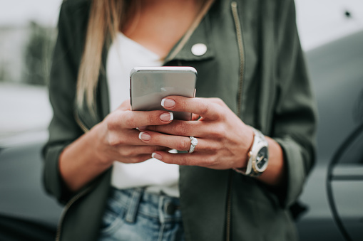 Close up female arm sending message on the phone while wearing contemporary watch and rings