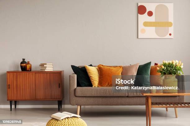Books And Vases On Retro Cabinet Next To Comfortable Sofa With Pillows Stock Photo - Download Image Now