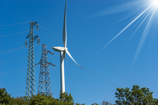 Wind turbine and high voltage towers (power line) on a clear blue sky with sun rays - Renewable energy concept