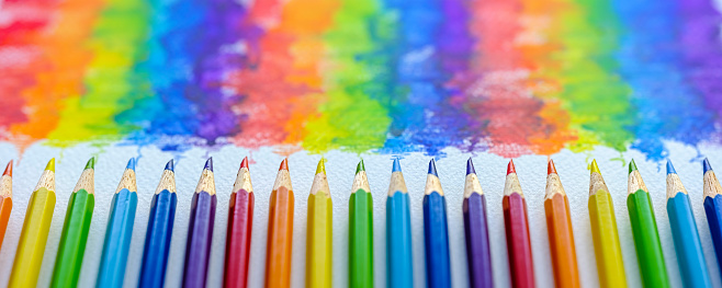 Vibrant rainbow colored water color coloring pencils or crayons in a row lying vertically with corresponding colorful shade drawing background, of the colors blending together, which features behind the crayons.. Concept image of people living together in harmony, mixing together, peace etc.