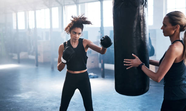 Getting in some extra practise Cropped shot of an attractive and athletic young female boxer working out with her trainer in the gym boxing stock pictures, royalty-free photos & images
