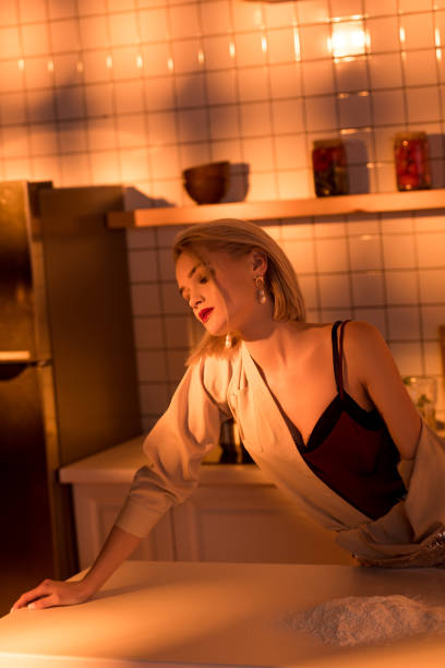 istock selective focus of elegant housewife leaning over counter while cooking in kitchen with orange light 1098287654