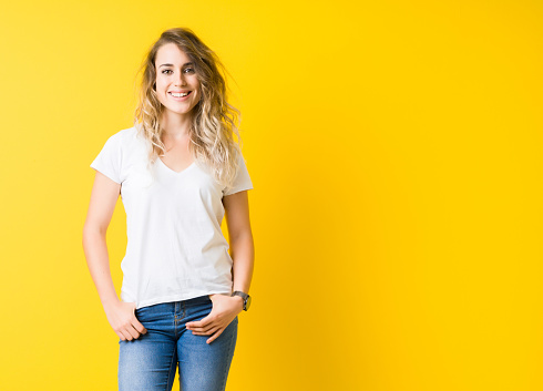 Beautiful young blonde woman smiling standing over isolated yellow background
