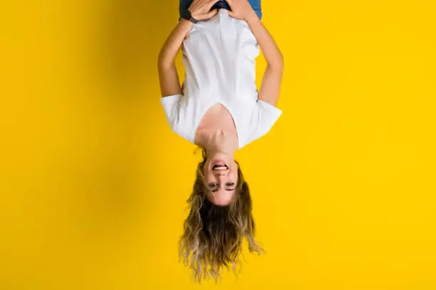 Photo of Beautiful young blonde woman jumping happy and excited hanging upside down over isolated yellow background