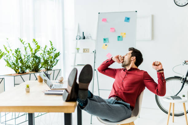 istock tired businessman with legs on table yawning in office 1098306148