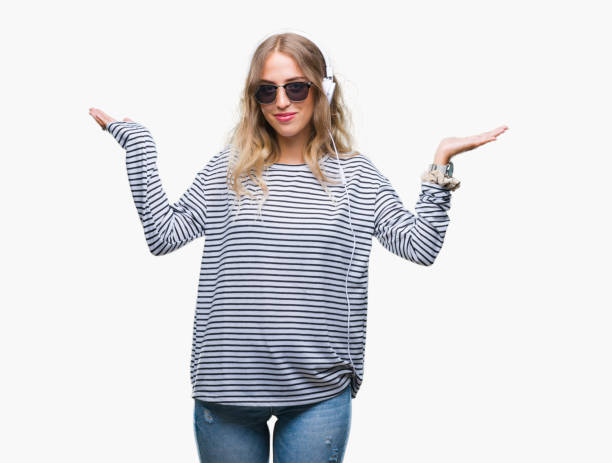 beautiful young blonde woman wearing headphones and sunglasses over isolated background clueless and confused expression with arms and hands raised. doubt concept. - head and shoulders audio imagens e fotografias de stock