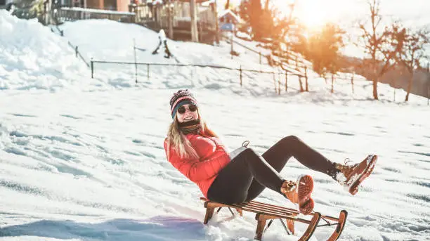 Young woman speeding with vintage sledding on snow high mountain - Happy girl having fun in white week vacation with chalet in background - Travel, winter sport, holiday concept - Focus on her face