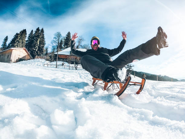 Young crazy man having fun with wood vintage sledding on snow mountain landscape - Happy guy enjoy winter vacation - Holiday concept - Focus on his face stock photo