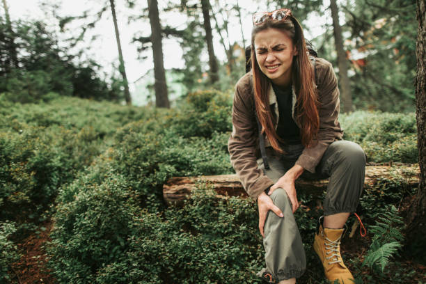 Young lady feeling pain in her knee while sitting on tree trunk