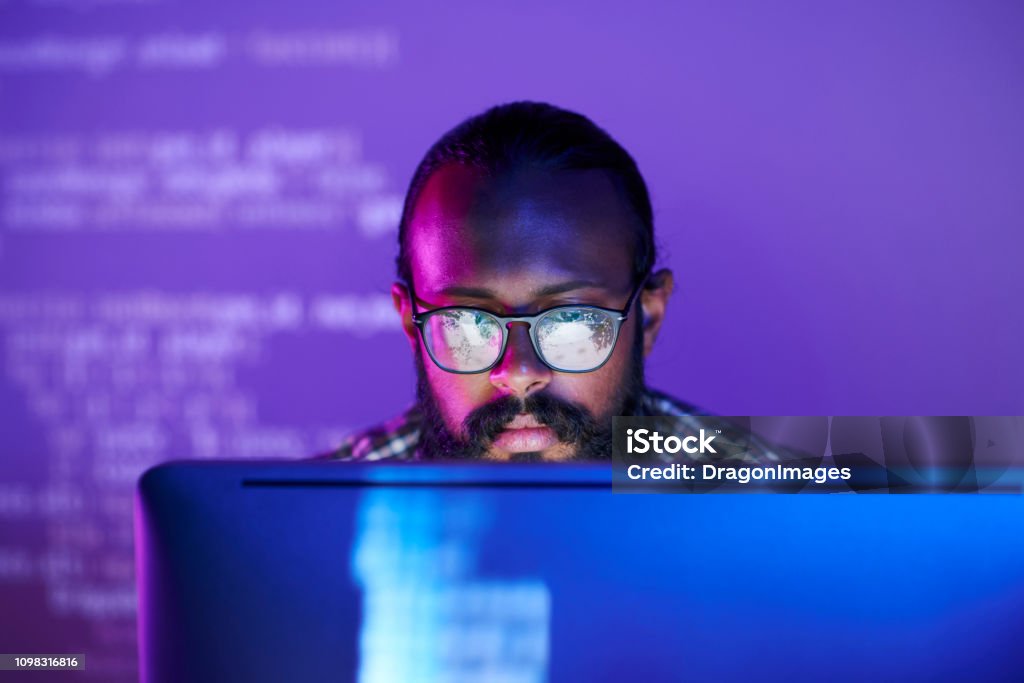 Programmer in front of monitor Young serious programmer in eyeglasses concentrating on working with coded data on computer screen Computer Programmer Stock Photo