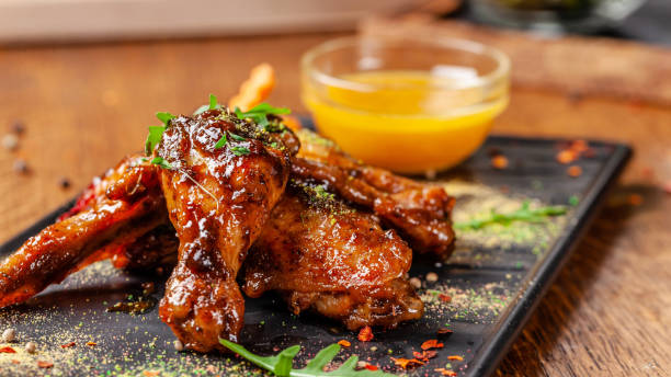 le concept de la cuisine indienne. ailes de poulet au four et les jambes dans une sauce moutarde et miel. servant des plats dans le restaurant sur une plaque noire. épices indiennes sur une table en bois. image de fond. - culture indienne dinde photos et images de collection