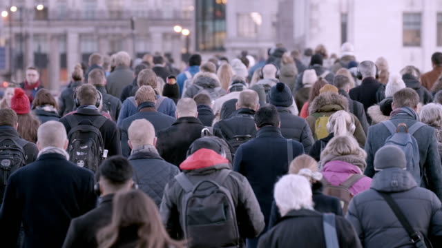 ロンドン橋を渡る通勤者の群衆は、多くの人々が寒い冬の朝に仕事に歩いて行く人々の多くの帽子と暖かい服を着ています。60fps。