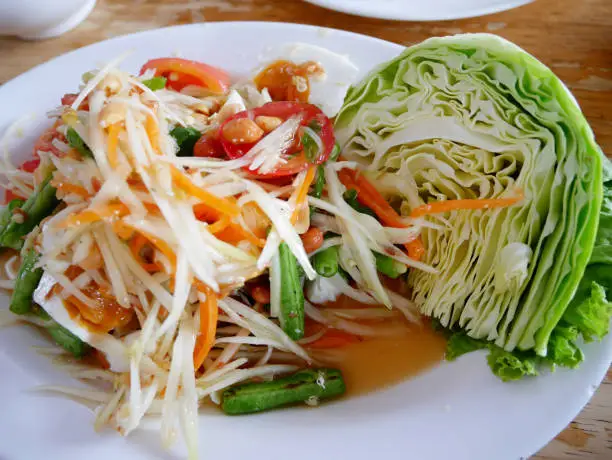 Photo of Thai cuisine Somtum or thai food fruit spicy green papaya salad with salted egg on dish serve with cabbage fresh vegetable