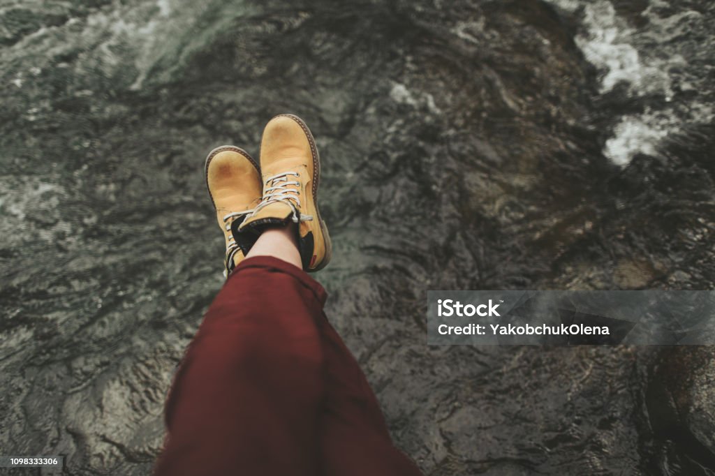 Close up of female feet over the stone river Close up of womans legs in touristic boots sitting on the river bank Timberland - Arizona Stock Photo