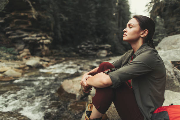 Young tired woman resting in the forest Peaceful young beautiful woman sitting on the stone near mountain river while resting after a long walk timberland arizona stock pictures, royalty-free photos & images