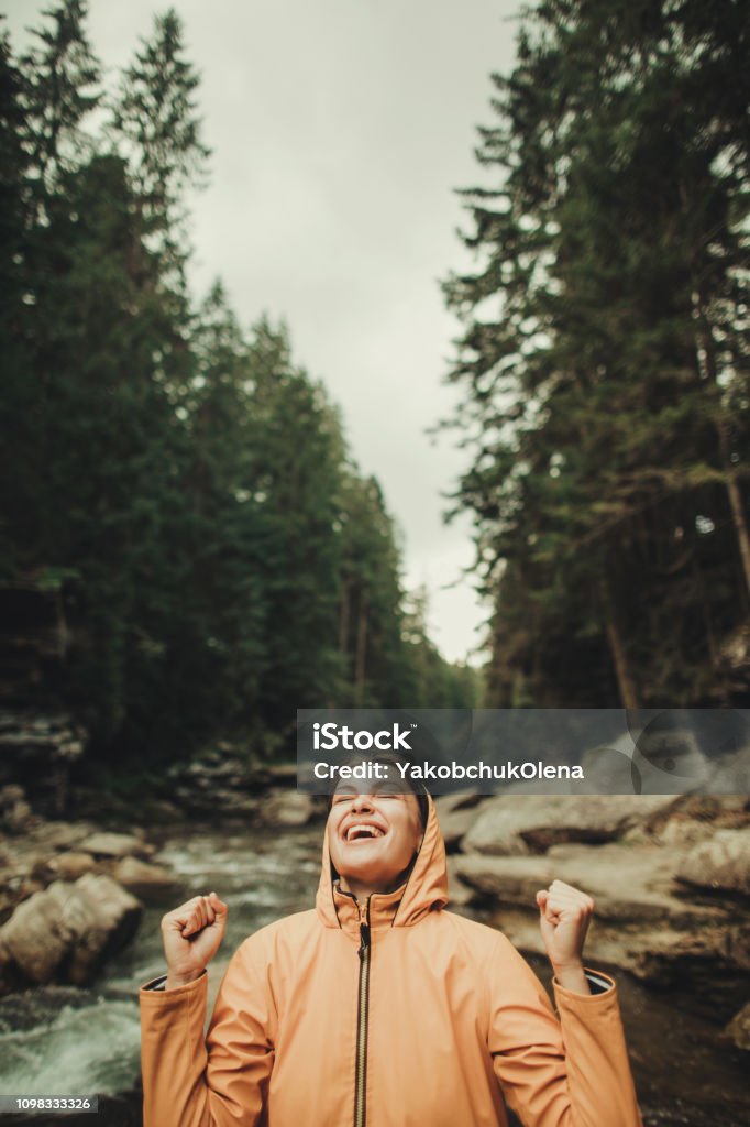 Delighted young woman feeling happy in the forest Happy attractive young woman standing near mountain river while enjoying her active weekend Adult Stock Photo