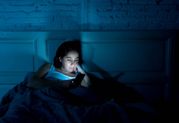 internet addicted giovane bella donna chiacchierando e navigando su internet utilizzando il suo smartphone assonnato annoiato e stanco a tarda notte nella dipendenza mobile e nel concetto di insonnia. - insonnia foto e immagini stock