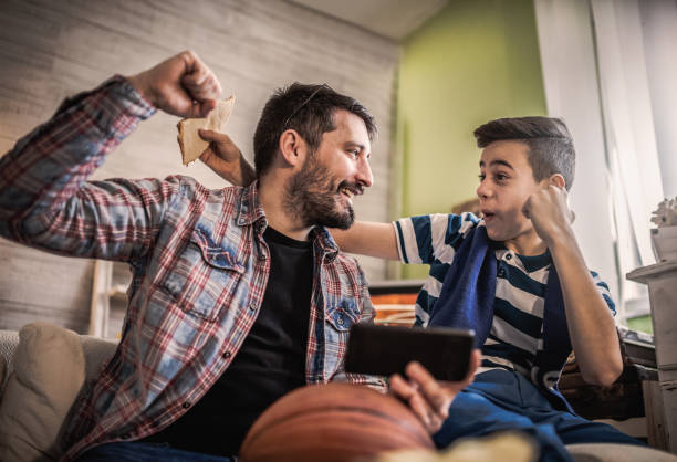 figlio felice e padre che tifano per la squadra di basket e guardano la partita a casa - hanging basket foto e immagini stock