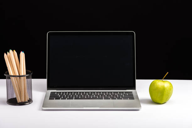 apple, laptop with blank screen and pencils isolated on black