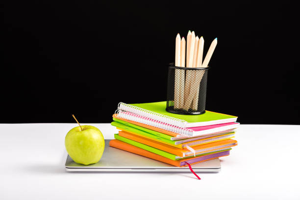 istock colorful notebooks, apple and laptop on desk isolated on black 1098347734