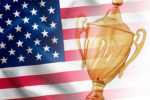 Gold trophy award superimposed on the national flag of USA in a concept of a championship win, the best, sport or competition