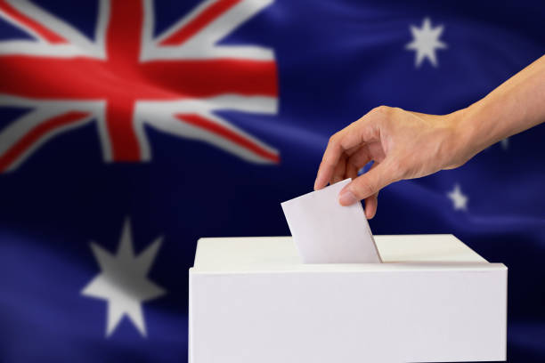 nahaufnahme der menschlichen hand gießen einfügen eine abstimmung und die wahl und entscheidung, was er will im polling-box mit australien flagge gemischt im hintergrund. - national arms stock-fotos und bilder