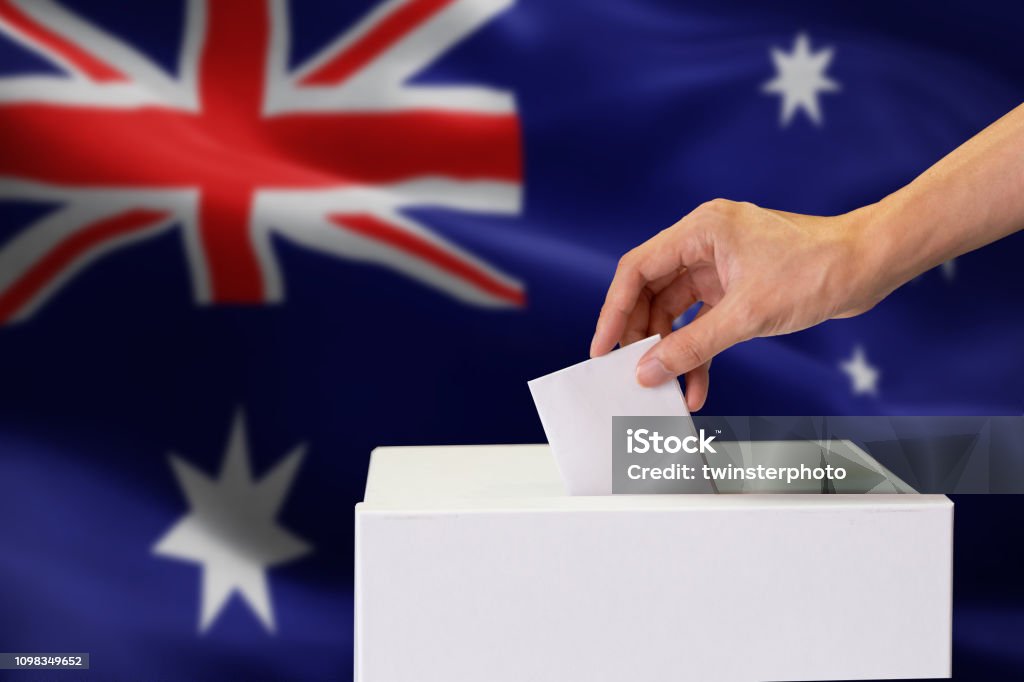 Primo piano del lancio a mano umano e inserimento di un voto e scelta e presa di una decisione ciò che vuole nel polling box con la bandiera australiana mescolata sullo sfondo. - Foto stock royalty-free di Australia