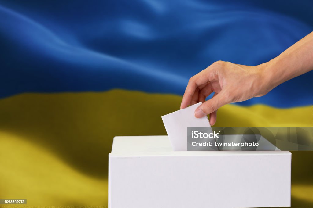 Close-up of man casting and inserting a vote and choosing and making a decision what he wants in polling box with Ukraine flag blended in background Close-up of man casting and inserting a vote and choosing and making a decision what he wants in polling box with Ukraine flag blended in background. Ukraine Stock Photo