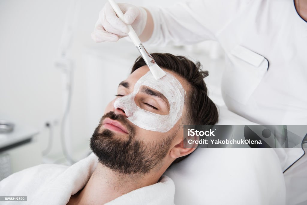 男性の顔に白い粘土のマスクをかけながらブラシを使用して美容師 - 男性のロイヤリティフリーストックフォト